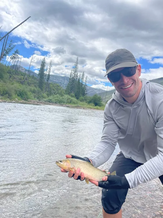 Zack holding a cutthroat trout beside a river in the Bob Marshall Wilderness, Montana